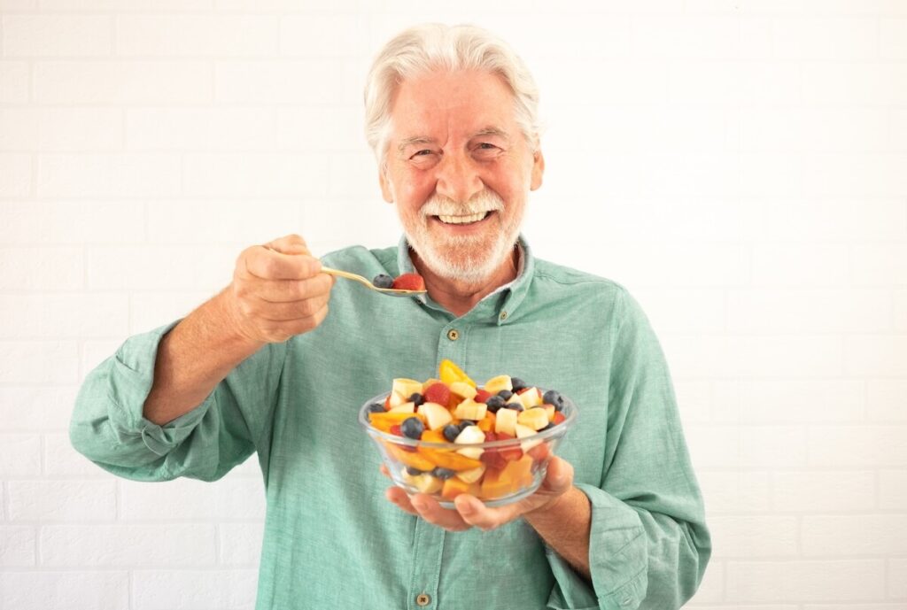 Older adult smiling and holing a healthy bowl of fruit