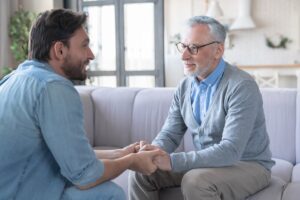 Adult son talking with his father while holding his hands